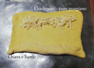 Impasto per il Khachapuri - pane georgiano steso sul piano di lavoro e con due strisce di formaggio lungo i lati lunghi. Un lato ripiegato sul formaggio.