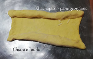 Impasto per il Khachapuri - pane georgiano steso sul piano di lavoro e con due strisce di formaggio lungo i lati lunghi. Entrambi i lati ripiegati sul formaggio.