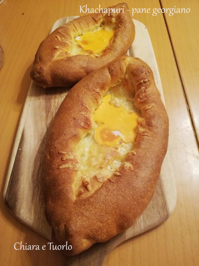 Due Khachapuri - pane georgiano cotti, appoggiati su un tagliere di legno e inquadrati di sbieco