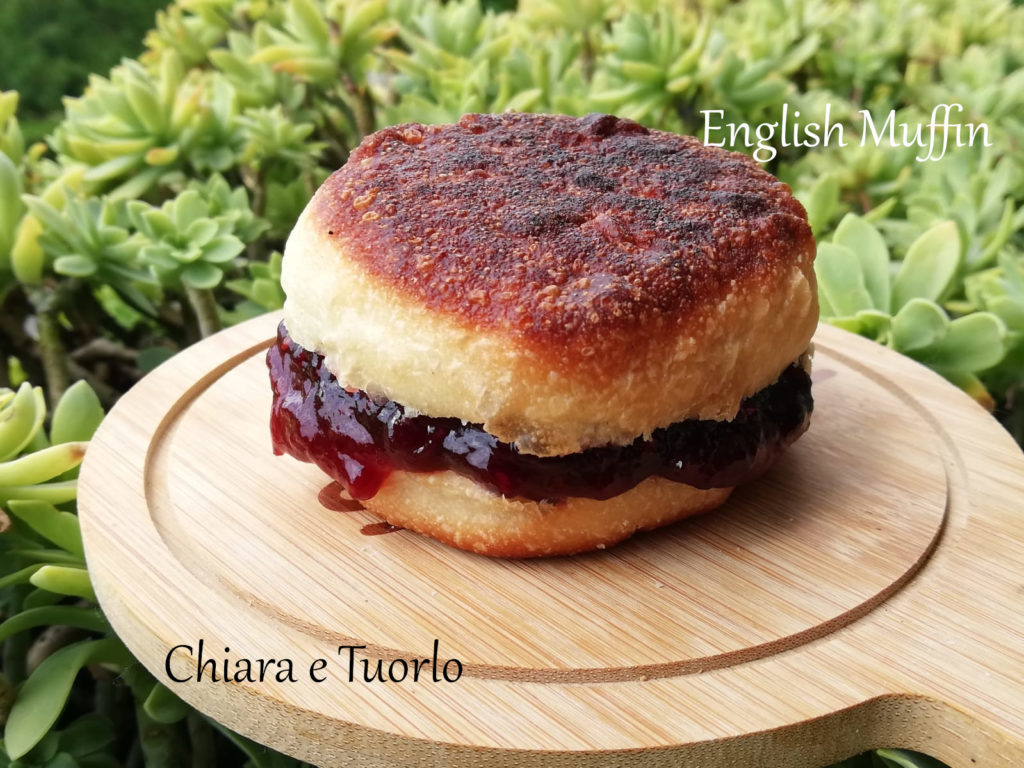 Un english muffin farcito con abbondante marmellata di frutti di bosco, posato su un piccolo vassoio di legno