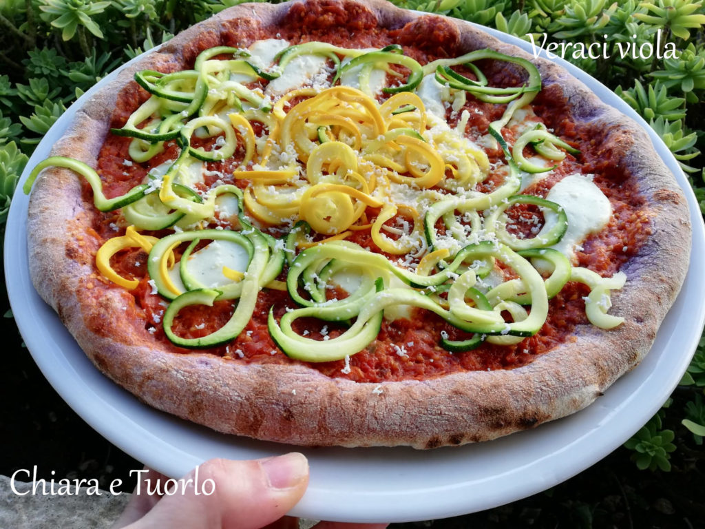 pizza verace viola cotta e appoggiata su un piatto, farcita con verdure miste molto colorate