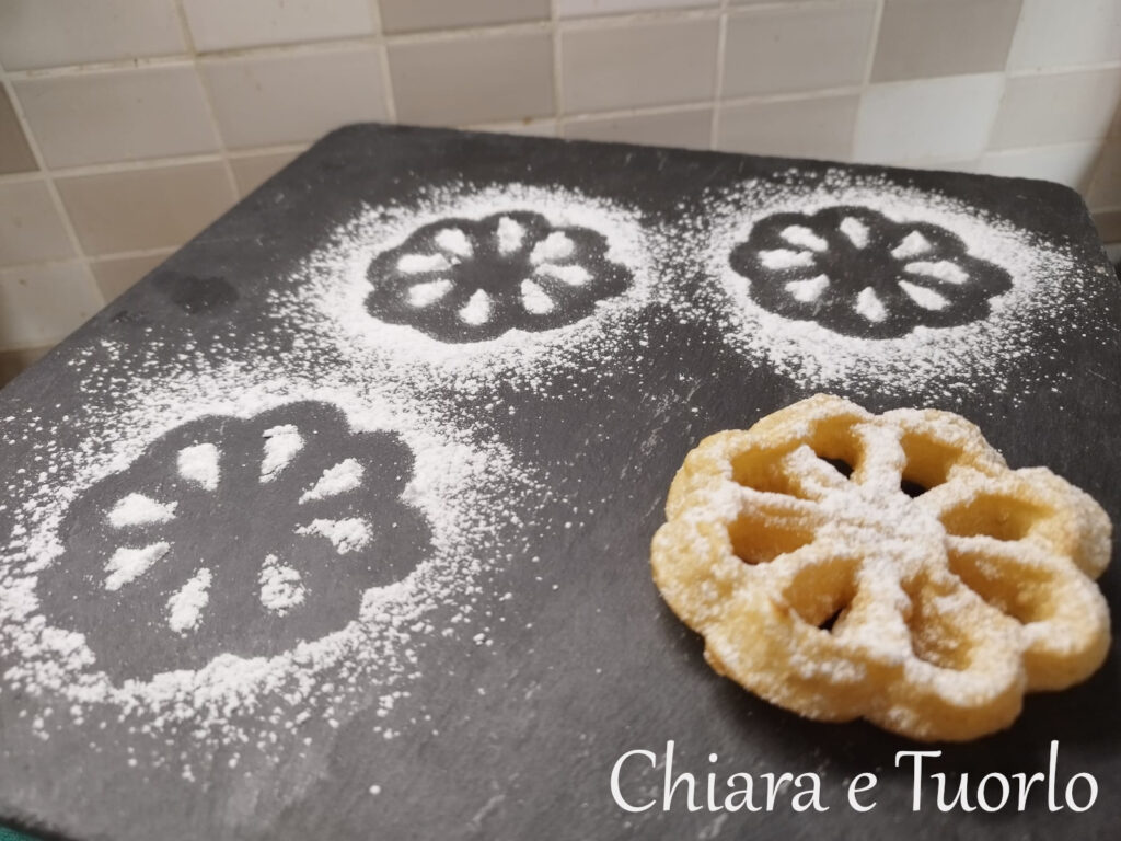 Una frittella a forma di fiore su un vassoio di ardesia con qualche disegno creato con lo zucchero a velo