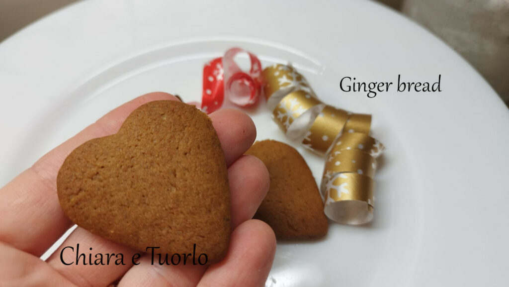 Ginger bread a forma di cuoricino tenuto in mano con il piatto sullo sfondo
