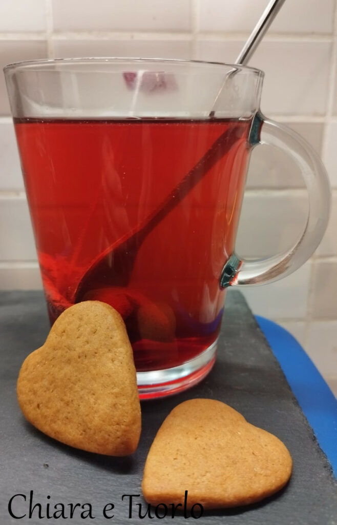 Tisana ai frutti di bosco in mug di vetro e un paio di biscottini a cuore appoggiati alla tazza